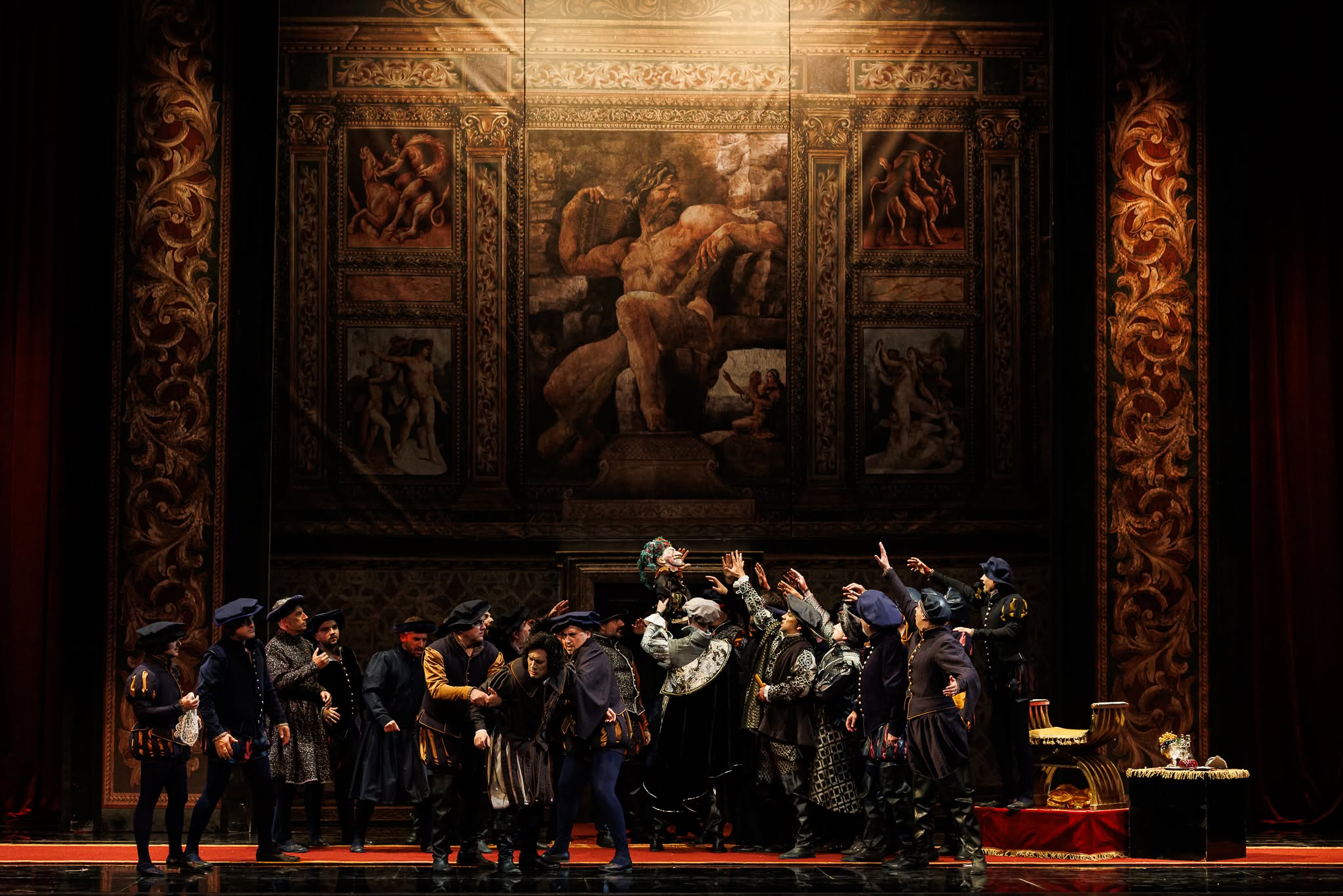 Group of opera singers in Renaissance attire standing under dramatic spotlight in front of a grand painted backdrop