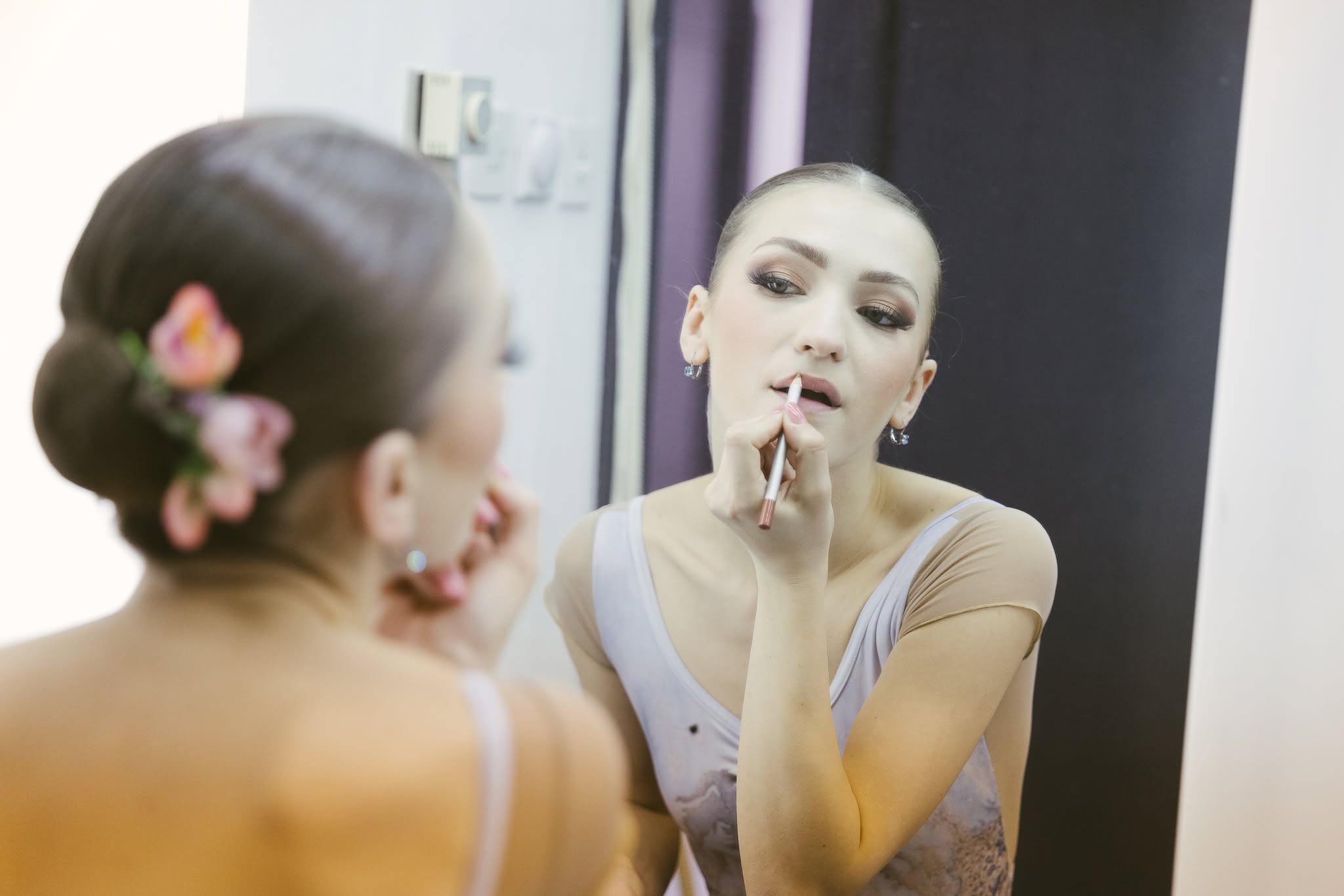 A female ballet dancer applying lip liner while looking in a dressing room mirror