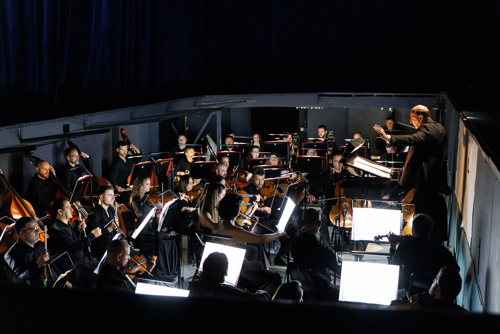 Conductor leading a symphony orchestra playing instruments inside a dark orchestra pit