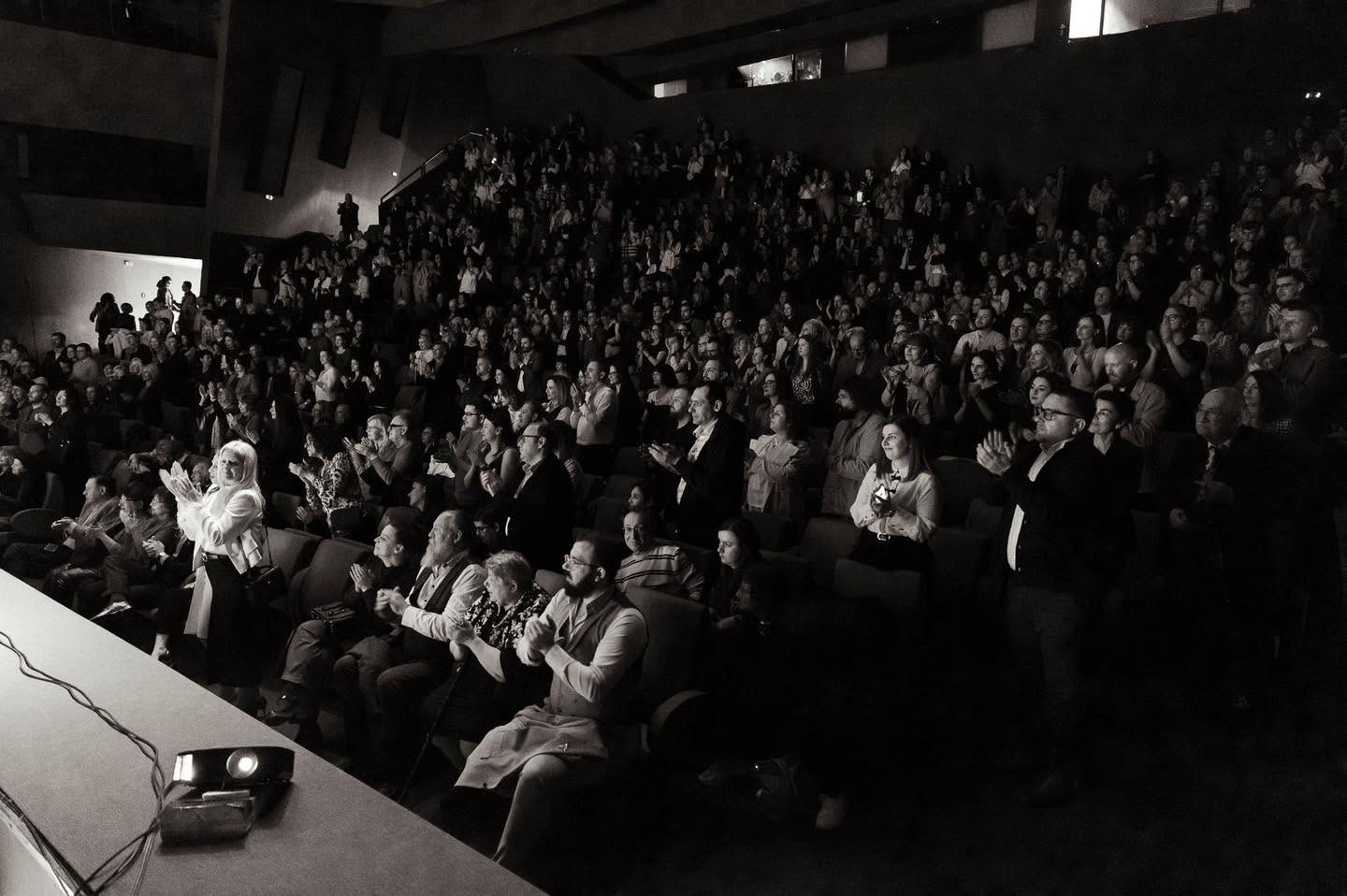 Black and white wide shot of a packed theater audience giving a standing ovation