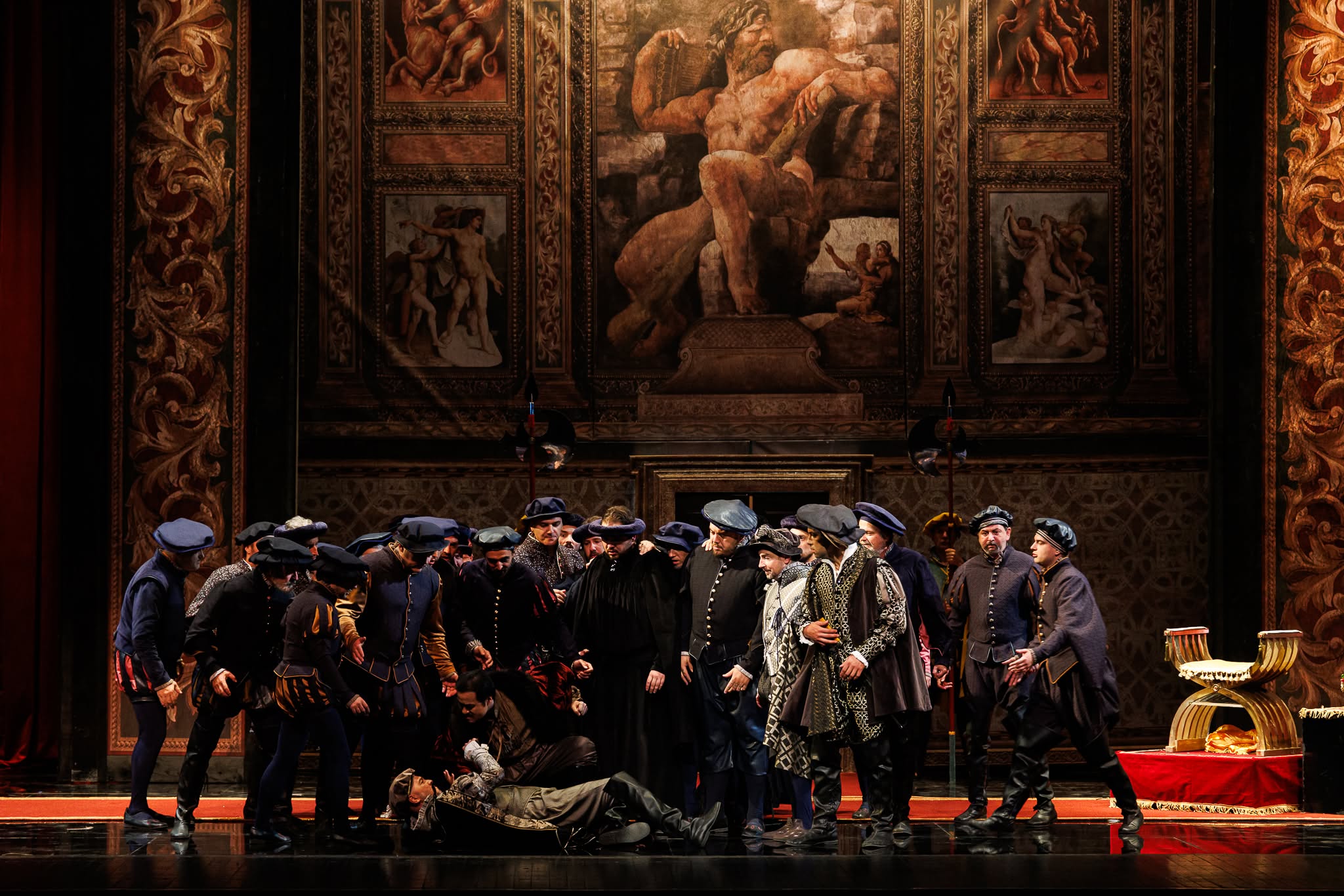 Group of male opera singers in Renaissance period costumes gathered around a fallen character on stage